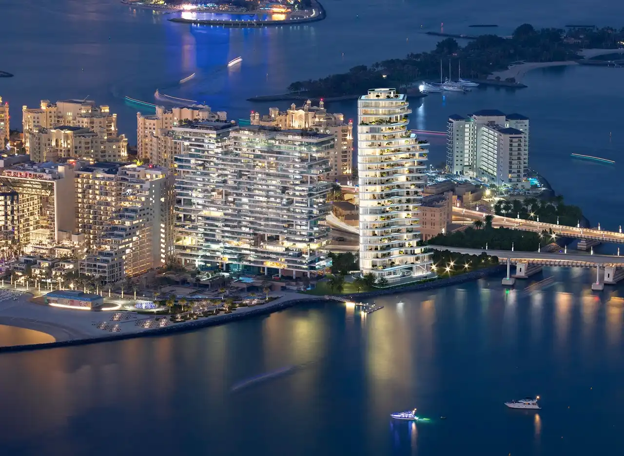 AVA at Palm Jumeirah, Dorchester Collection by OMNIYAT illuminated waterfront tower and surrounding coastal skyline at night in Dubai Presented by Tohid Fetrat