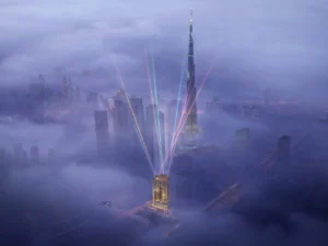 Elegance Tower by DAMAC in Downtown Dubai with illuminated tower design and Burj Khalifa skyline emerging above the clouds in Dubai - Presented by Tohid Fetrat