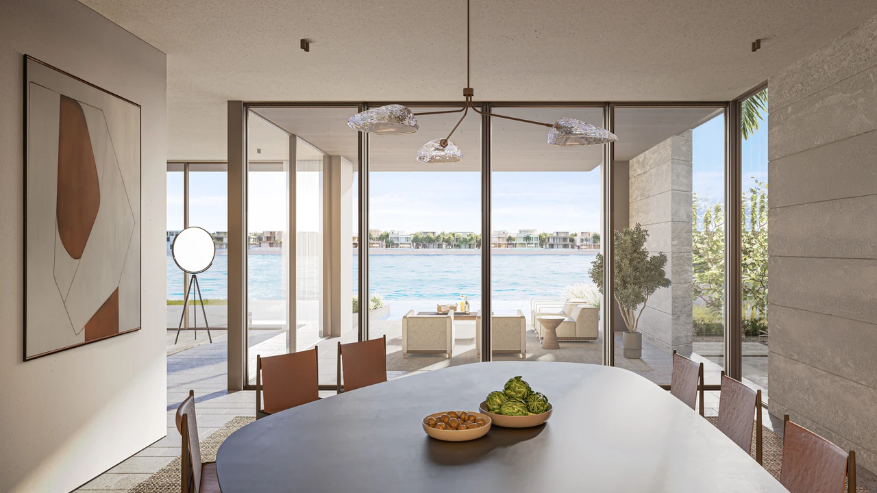 Frond A by Nakheel in Palm Jebel Ali Cobalt villa dining area with oval table sculptural pendant lighting wall art and waterfront glazing in Dubai - Presented by Tohid Fetrat