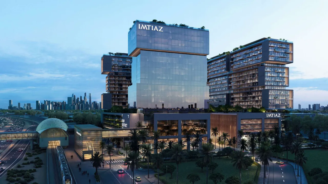 RAW District by Imtiaz in Downtown Jebel Ali evening exterior view featuring residential towers, office building, metro station, and landscaped surroundings in Dubai - Presented by Tohid Fetrat