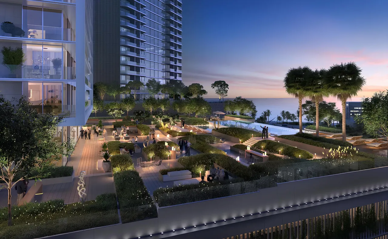 Saria by Beyond in Dubai Maritime City podium garden terrace at dusk with lit walkways clipped hedges pool deck and an open sea horizon in Dubai - Presented by Tohid Fetrat